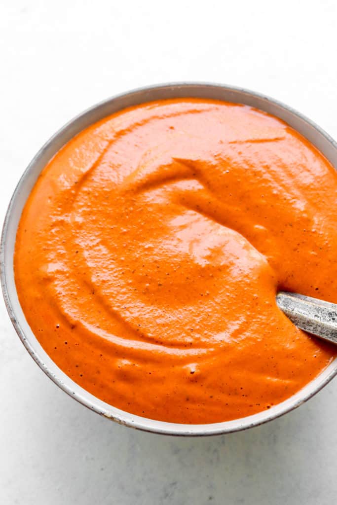 Round bowl filled with orange red pepper sauce with a silver spoon sticking out of it