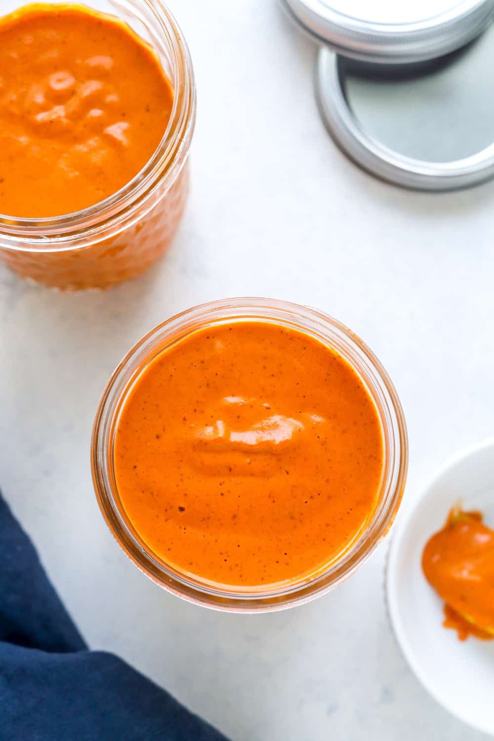overhead view of mason jar filled to the top with orange sauce with another one behind it and a dark blue towel next to it.