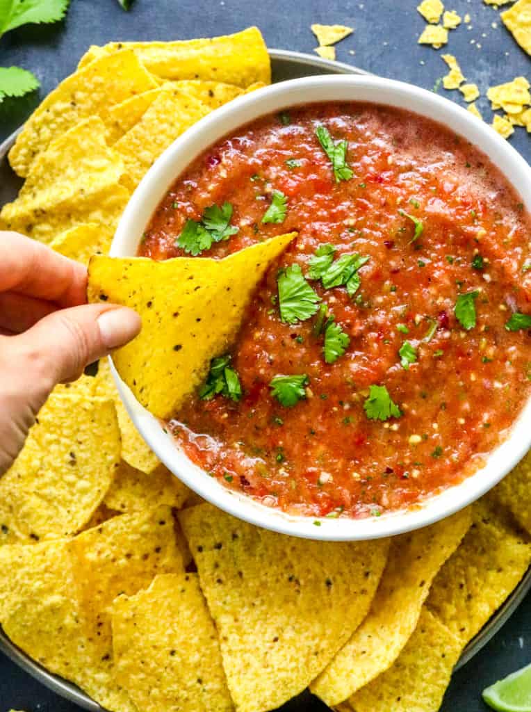 hand dipping a tortilla chip into a white bowl filled with fresh tomato salsa
