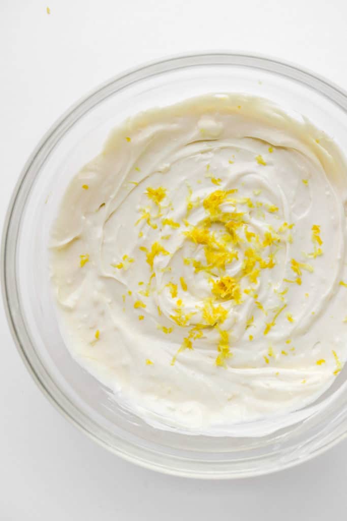 Round glass bowl filled with creamy whipped topping with lemon zest on top of it