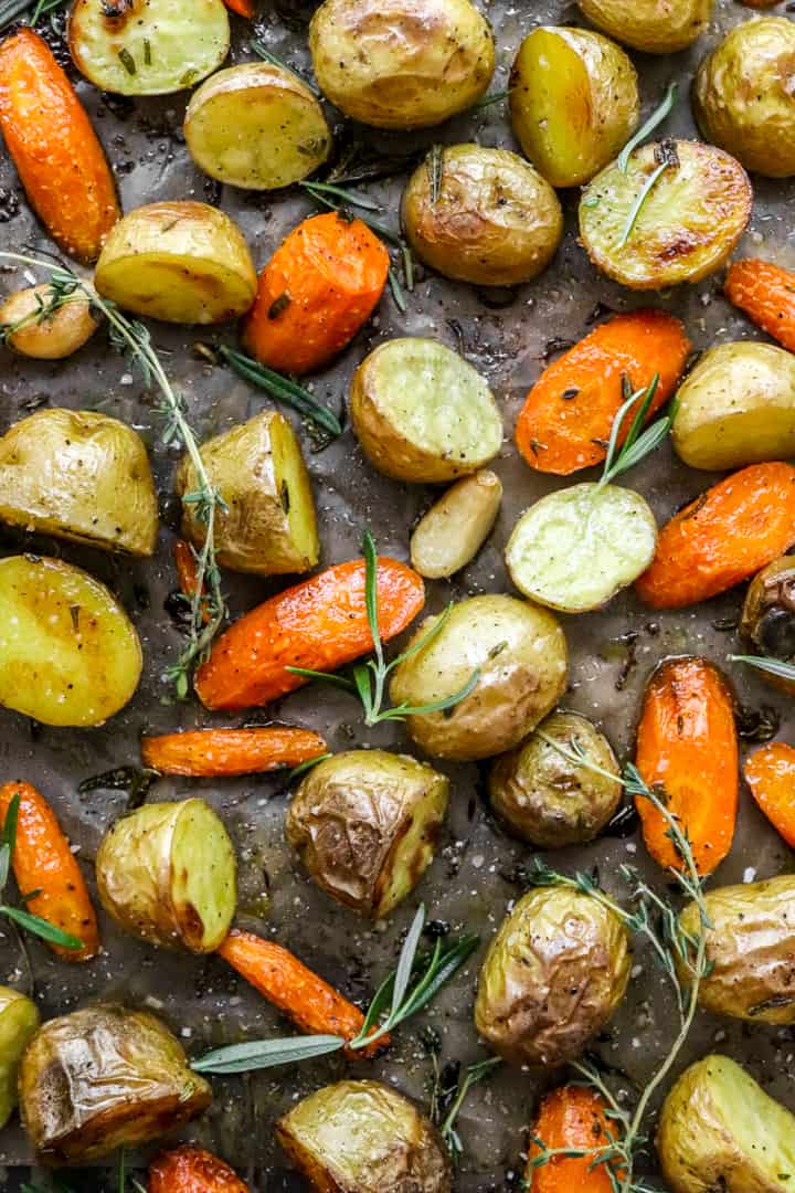Sliced baby potatoes and carrots on a pan with fresh sprigs of herbs on them. 