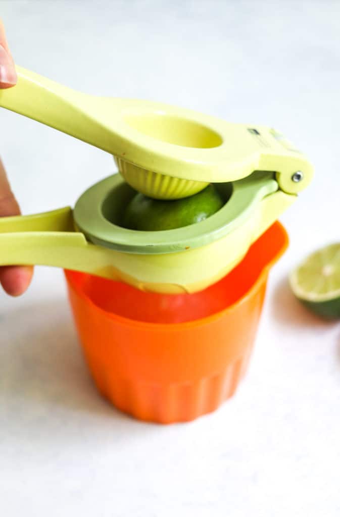 A yellow hand juicer squeezing lime juice out of a lime over an orange cup