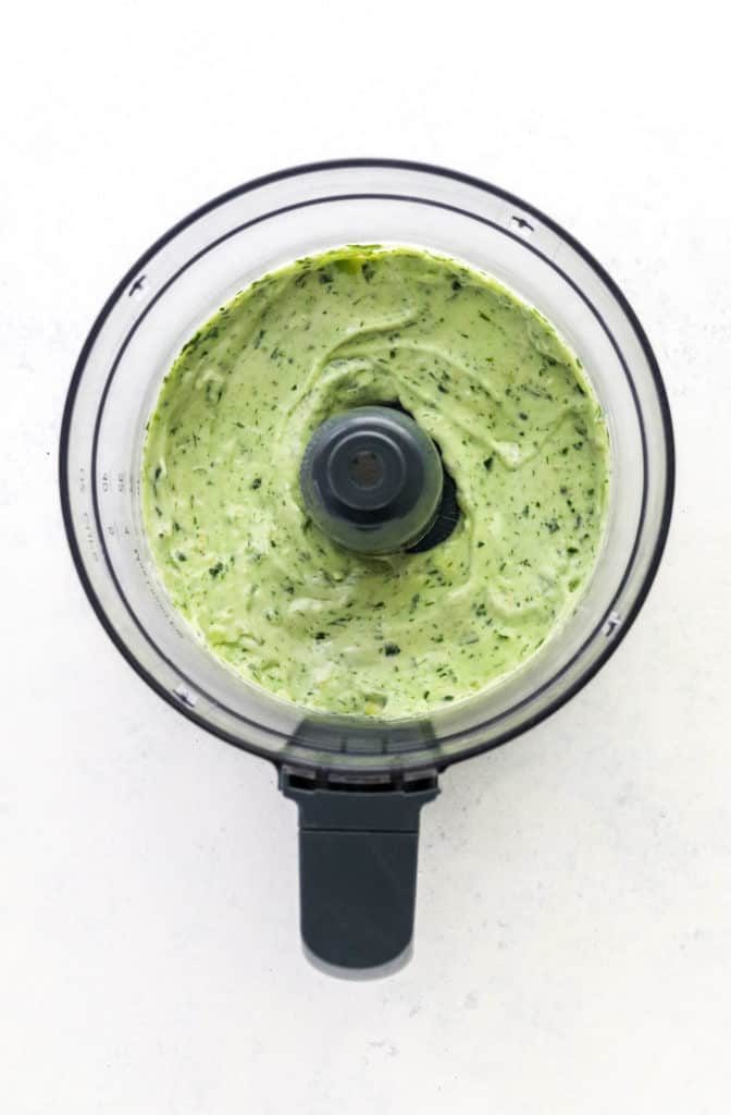 Blended creamy green avocado dressing in the bowl of a food processor