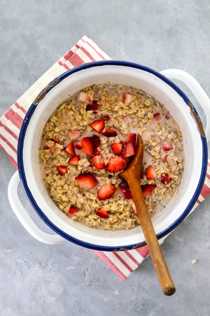 round pot with creamy oatmeal in it topped with chopped strawberries with a wooden spoon in the pot