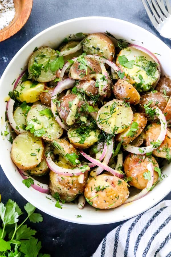White serving bowl with potato salad in it topped with sliced onion and herbs