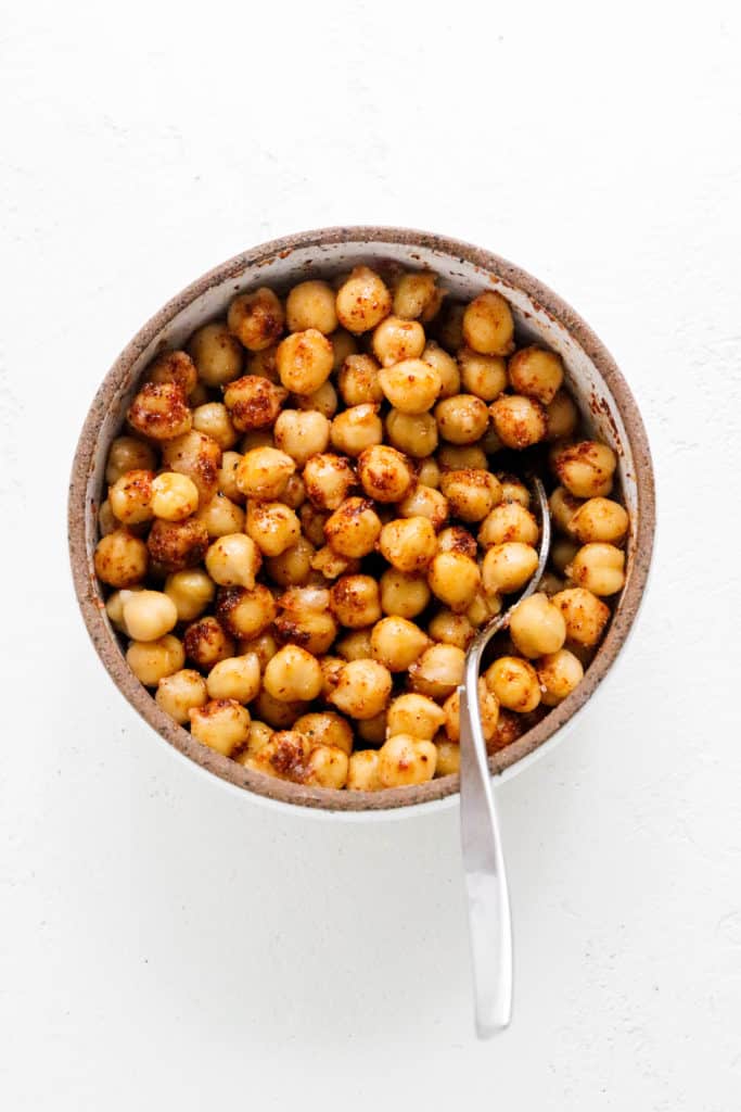 Round cream bowl filled with seasoned chickpeas with a silver spoon in the bowl