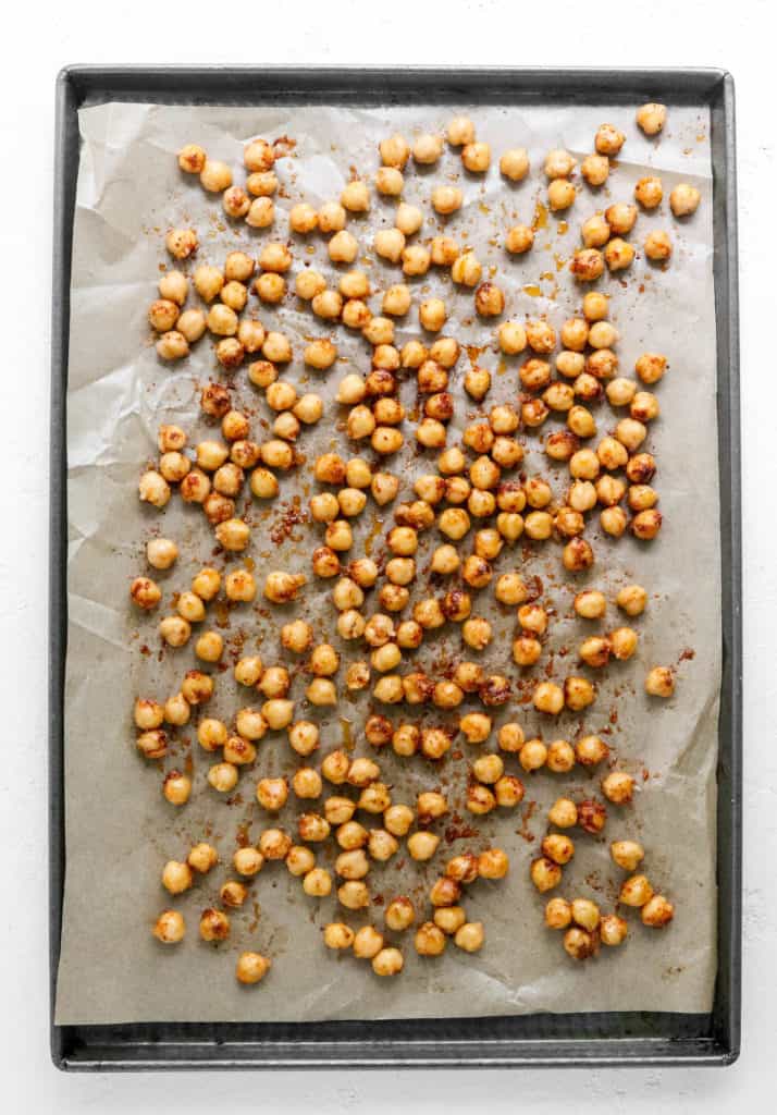 Metal pan with brown parchment paper on it with seasoned chickpeas spread over the paper