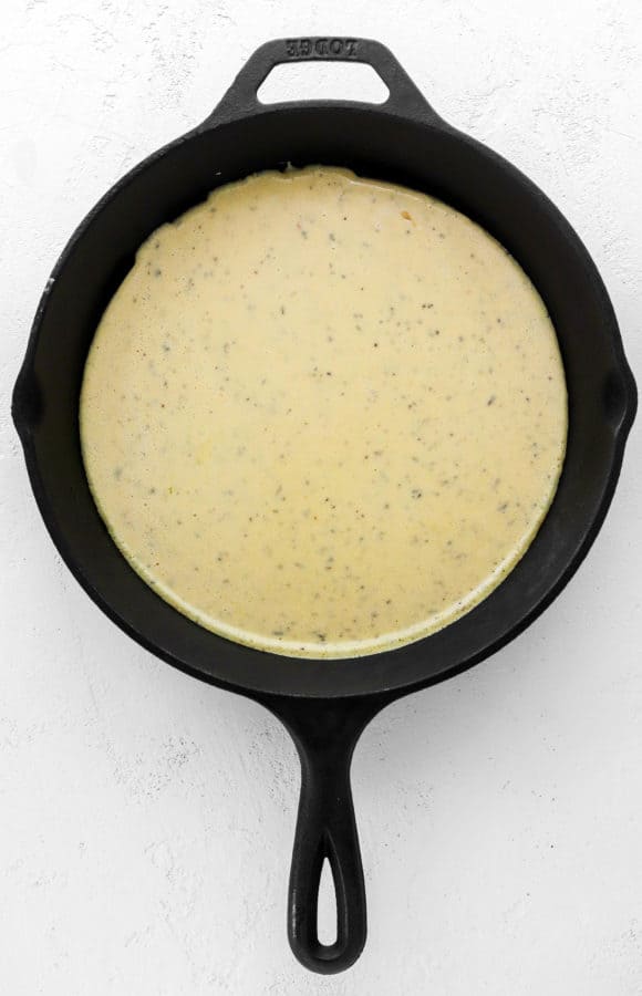 Chickpea flour pizza batter in a black pan on a white surface
