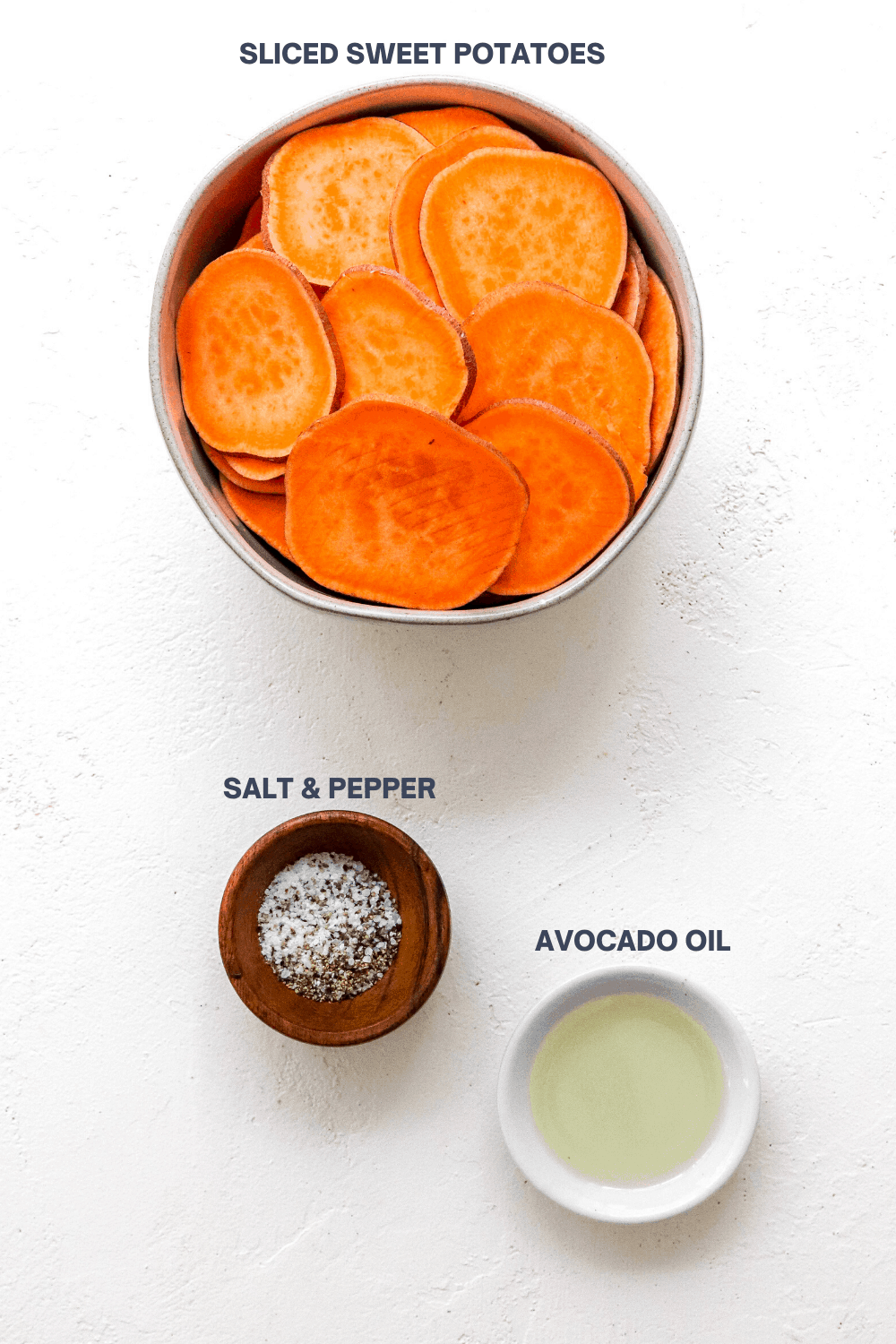 Round bowl filled with sliced sweet potato with a brown bowl filled with salt and pepper and a small white bowl with oil in it in front of it on a white surface. 