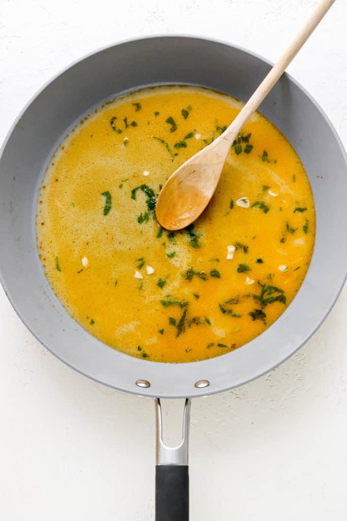 Grey pan with a yellow sauce and a wooden spoon in it on a white surface