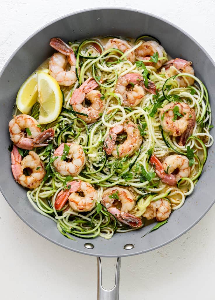 Grey pan with healthy shrimp scampi in it with zucchini noodles, shrimp in it with a couple lemon wedges on the side