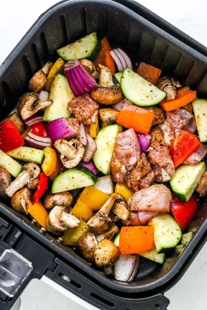 Uncooked chicken and vegetables in an air fryer basket.