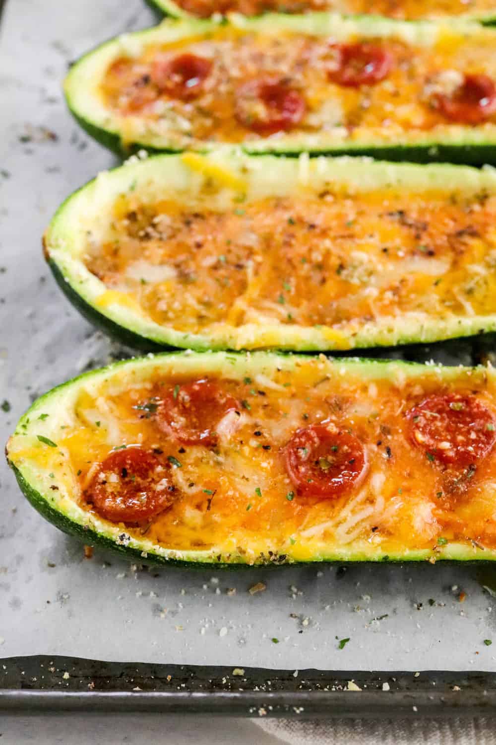 Close up of zucchini pizza boats on a lined baking sheet with pizza seasoning on them. 