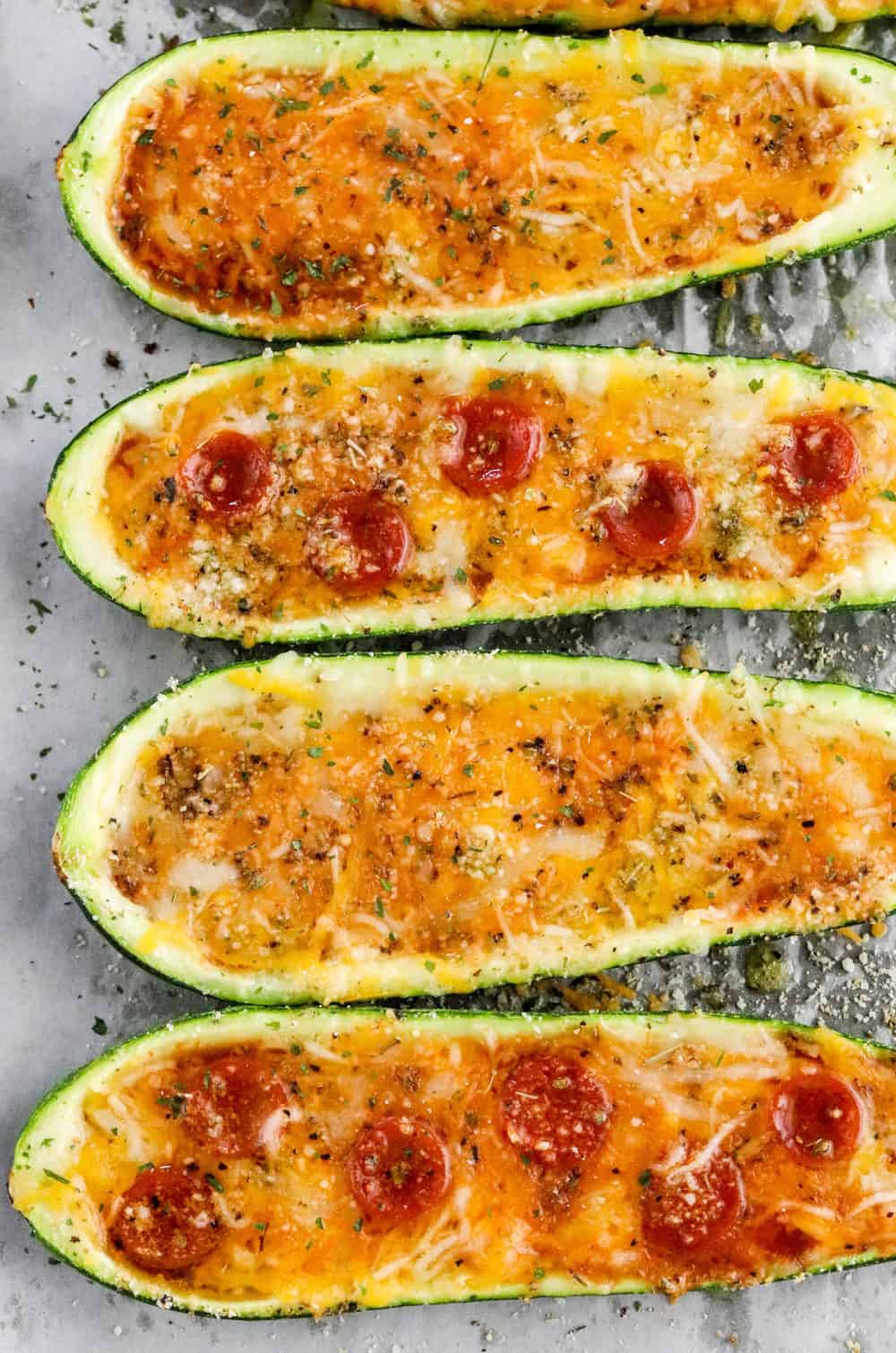 4 pizza filled zucchini lined up on a baking sheet. 