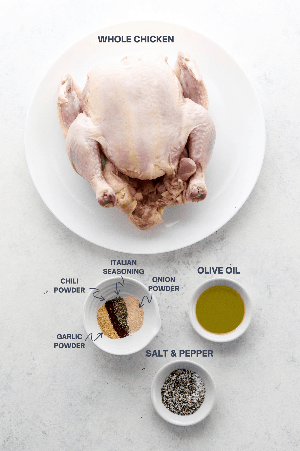 A whole, raw chicken on a round white plate with a bowl of spices and a small bowl of oil and bowl of salt and pepper in front of it with labels for these ingredients over the top of each item. 