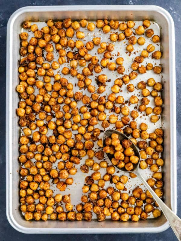 Silver sheet pan with crispy cooked chickpeas on it with a spoon on the pan.