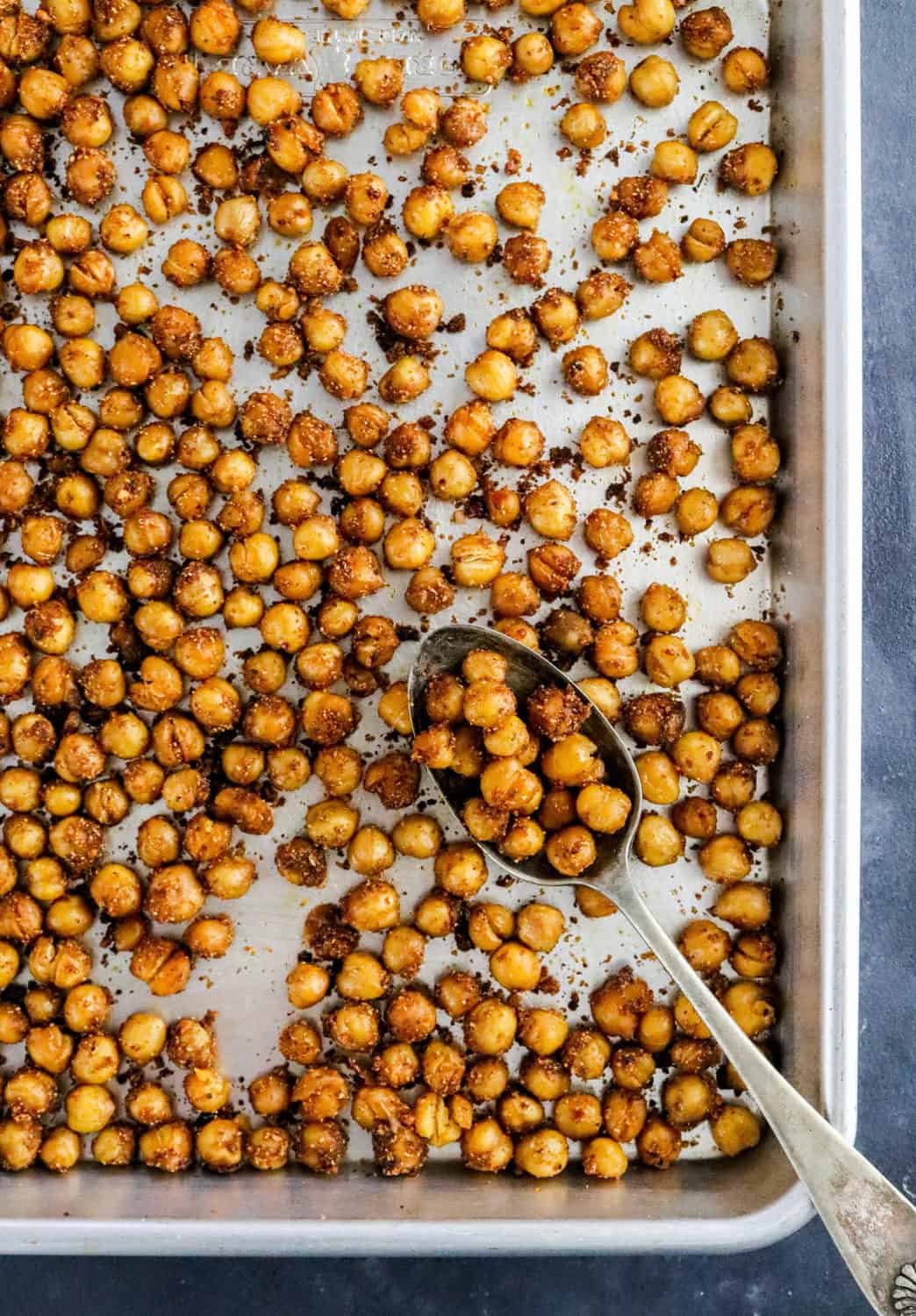 Crispy chickpeas roasted on a silver pan with a spoon on the pan with some chickpeas on it. 