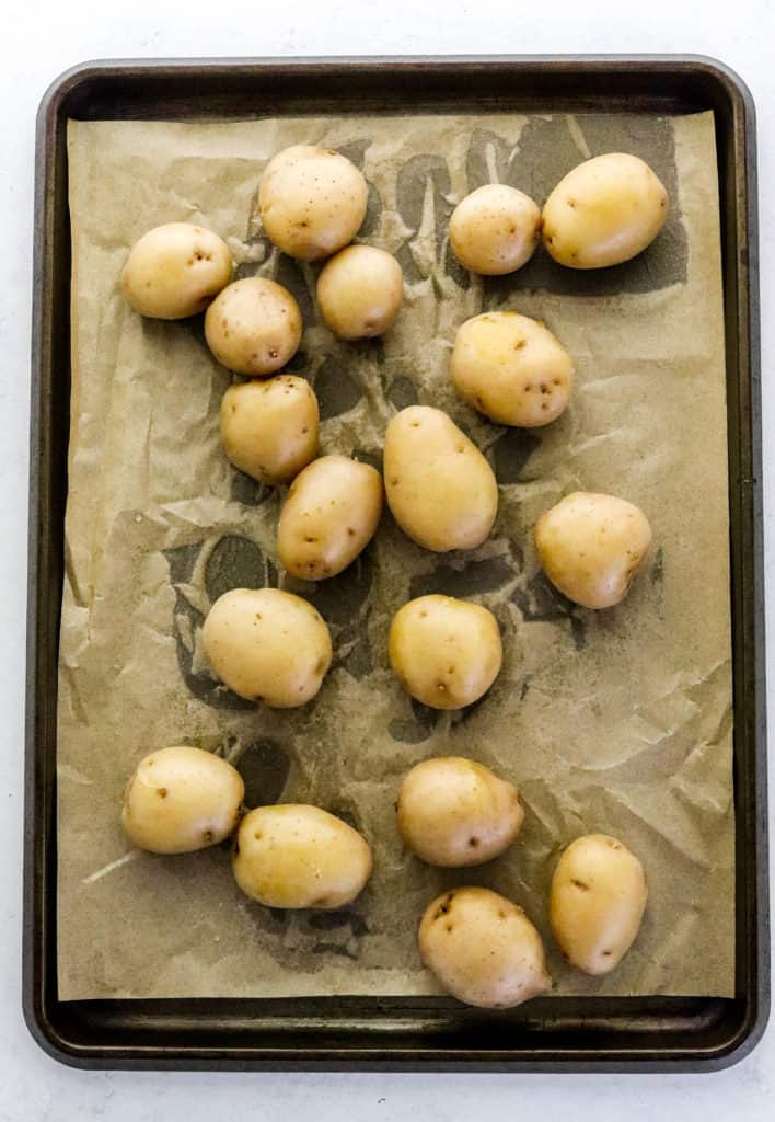 Dark brown baking sheet with brown parchment paper on it with cooked brown baby potatoes on top of the parchment paper