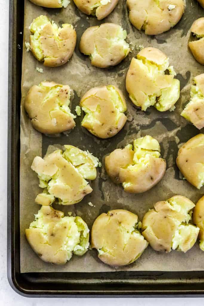 Baking sheet with brown parchment paper on it with smashed brown baby potatoes on it