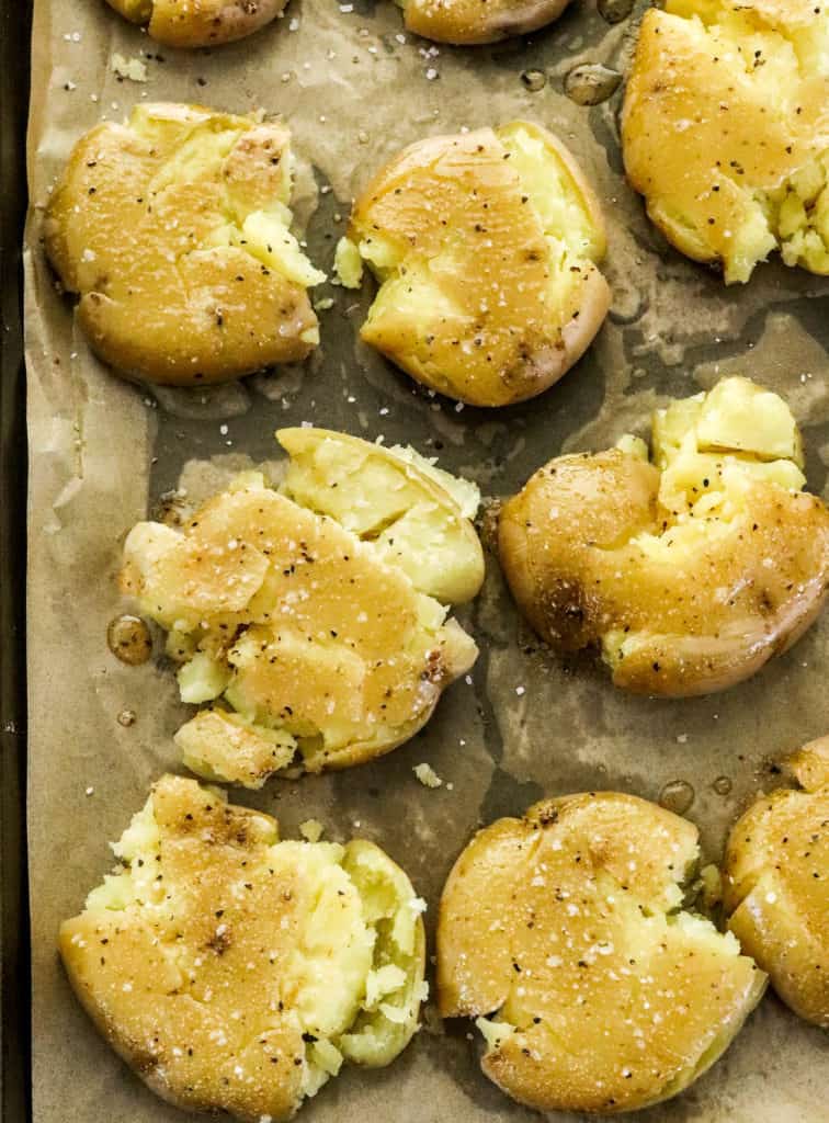 A bunch of smashed gold potatoes on a baking sheet covered in oil and seasoning