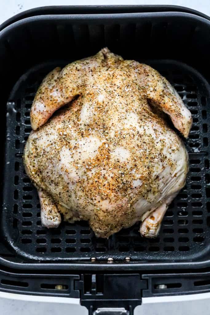 Seasoned, whole, raw chicken  in a black, square air fryer basket