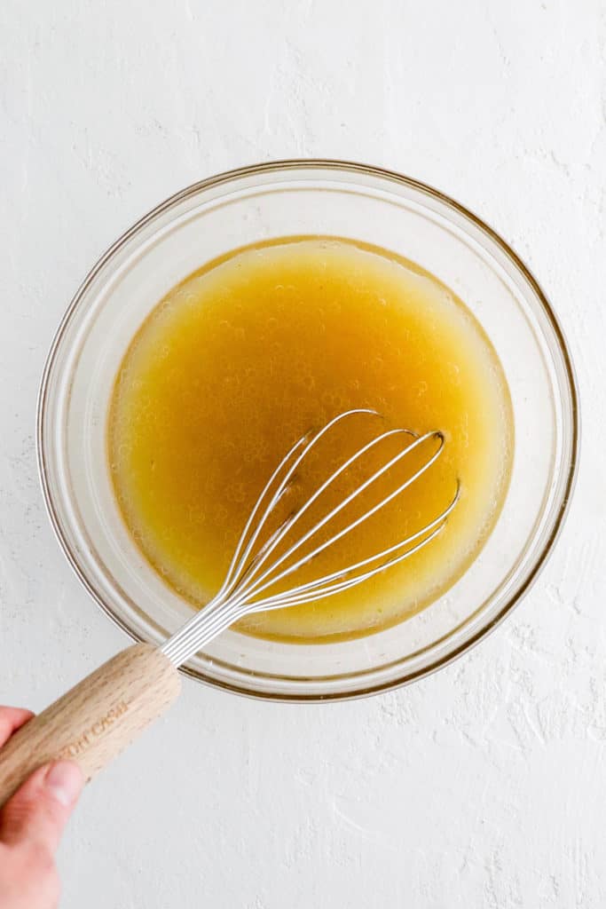 Round glass bowl filled with a yellow liquid mixture with a whisk in the bowl