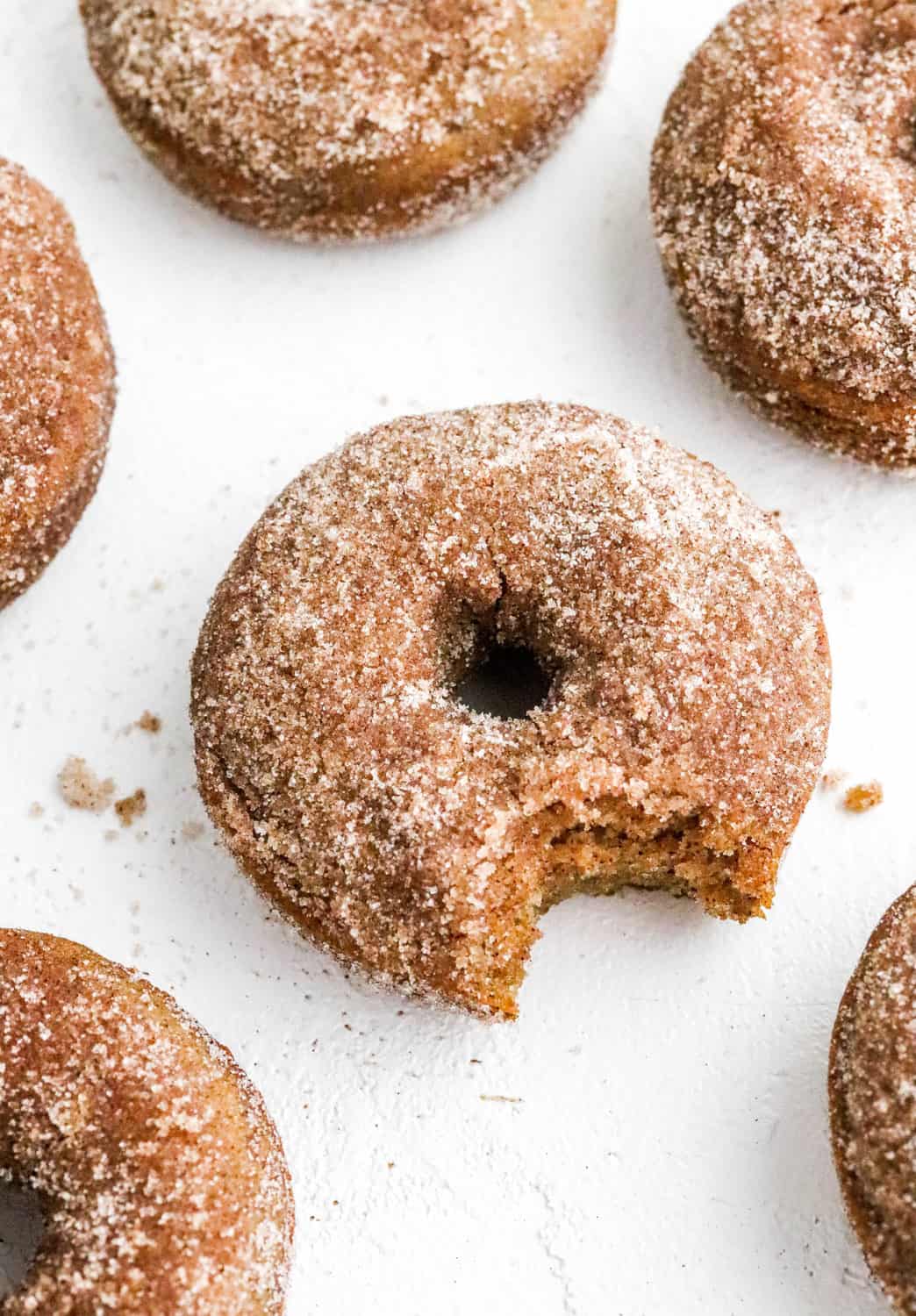 Healthy cider donuts laid out on a white surface with cinnamon Sugar on them. 