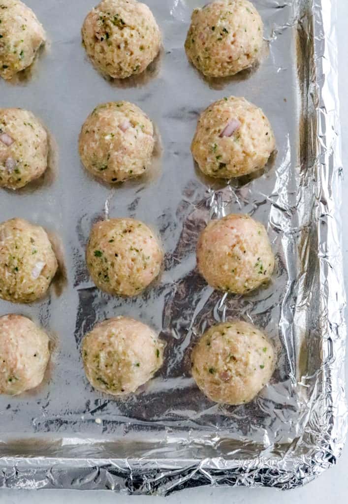 Uncooked rolled turkey meatballs on a foil lined pan