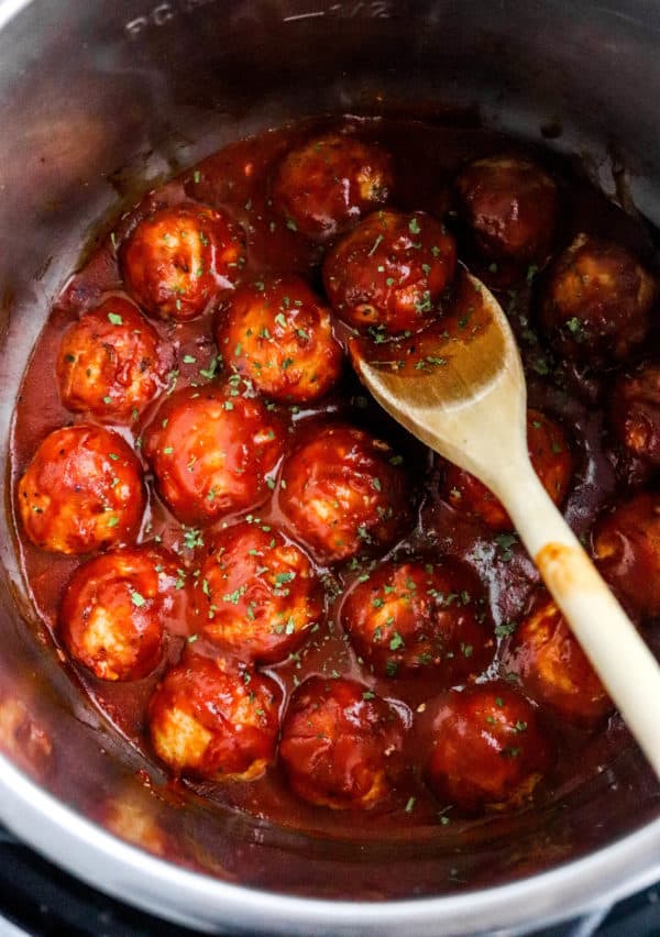 Simmered meatballs in bbq sauce in a pot with a wooden spoon storing the meatballs in the pot