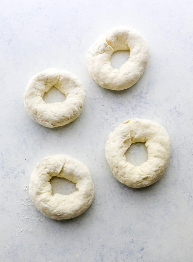 4 pieces of raw, uncooked bagel dough on a counter. 