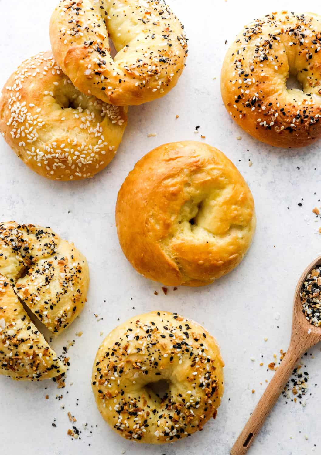 Plain bagel with more bagels with seasoning on them around it on a white surface. 