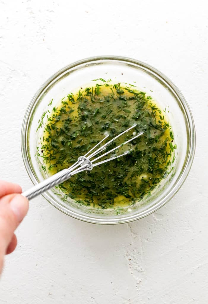 Hand whisking a lemon and dill marinade  in a small round glass bowl