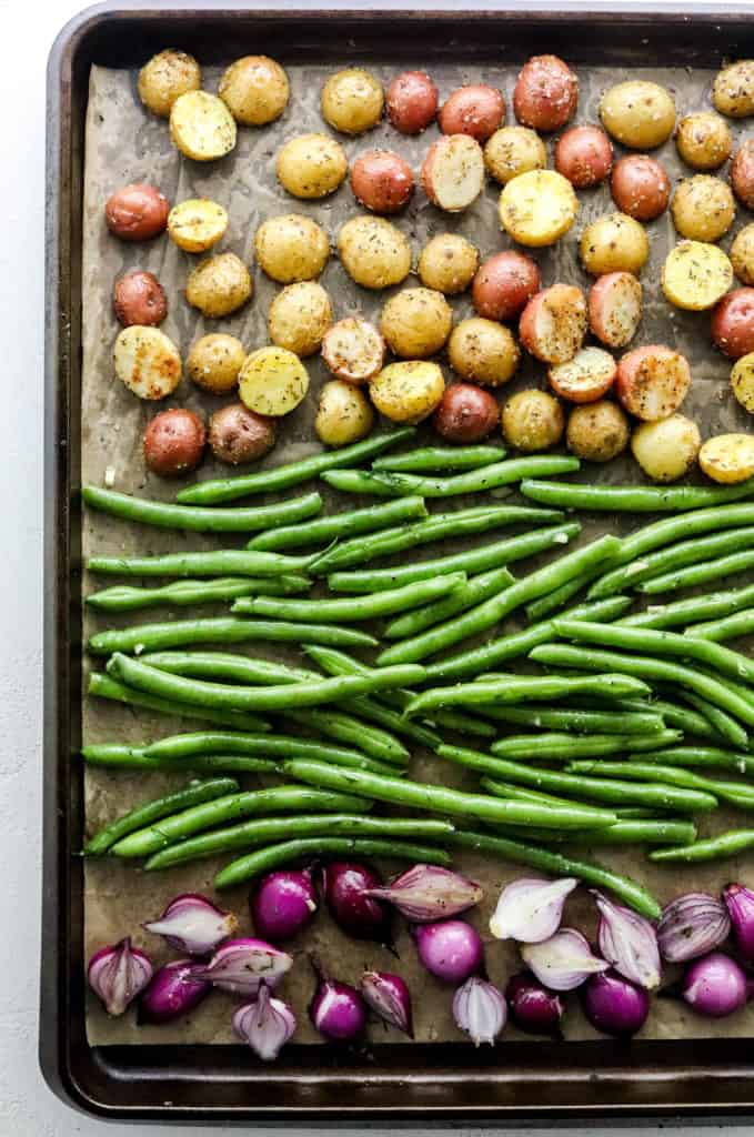Sheet pan with sliced babu potatoes, green beans and purple onion separated on the pan 