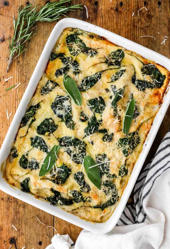Baked white squash and spinach lasagna in a white baking dish on a wooden surface