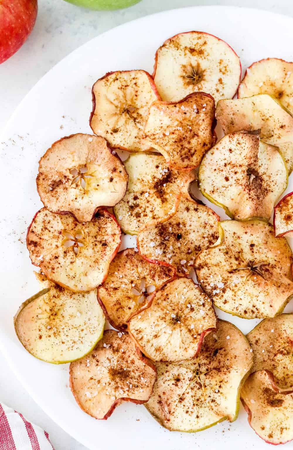 Crispy air fryer apple chips sprinkled with cinnamon and seas salt spread out on a round white plate