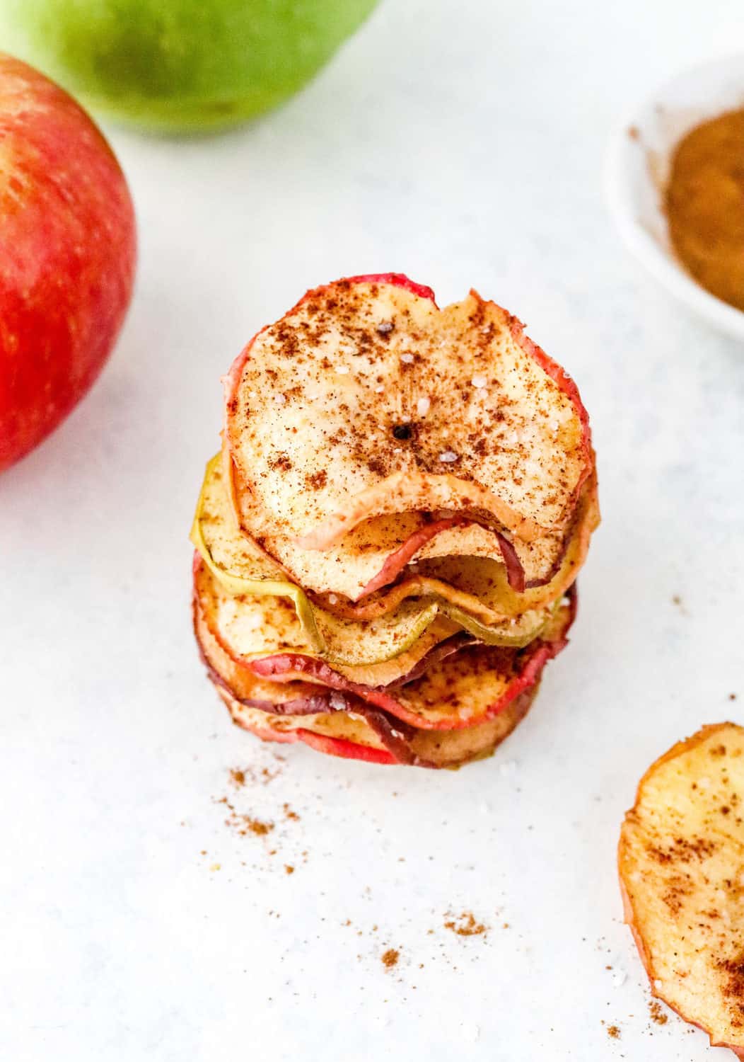 stack of crisp apple chips with a red and green apple behind it.