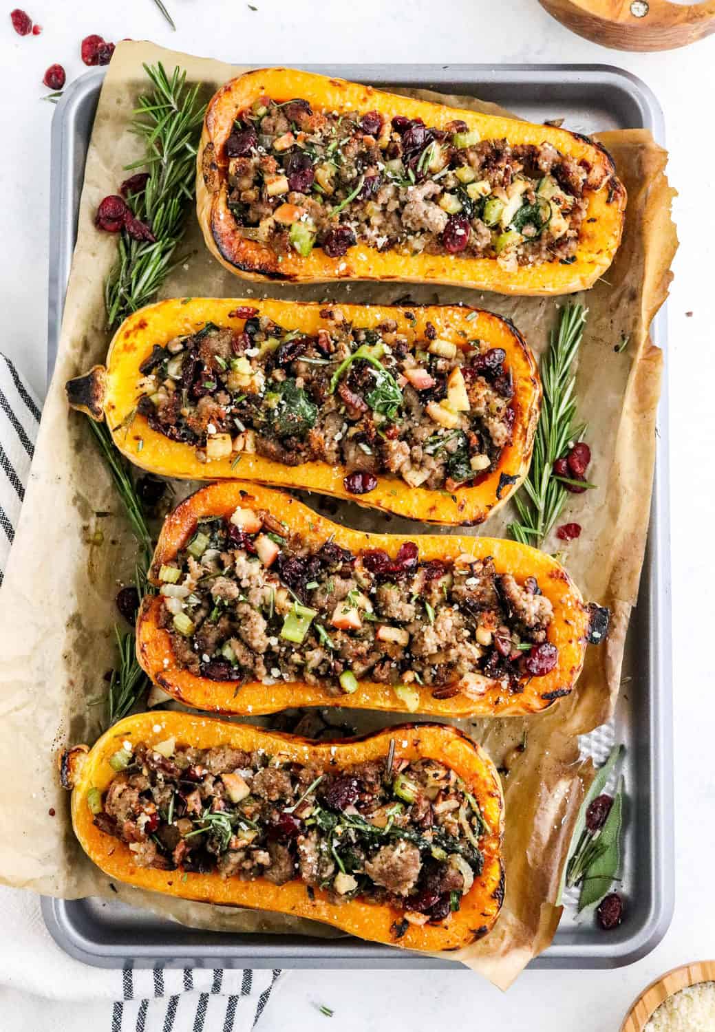 Baking sheet lined with brown parchment paper with halves of butternut squash filled with a sausage stuffing on it. 