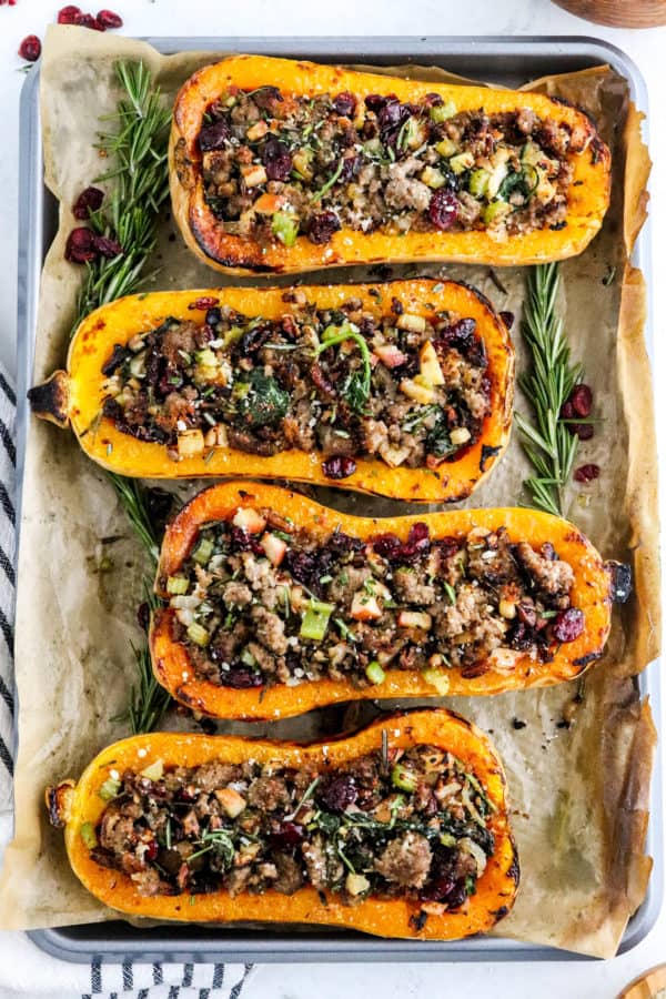 Roasted butternut squash stuffed with sausage and apples on a baking sheet with fresh rosemary around it