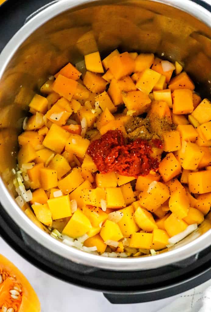 Cooked cubed squash and onions in an instant pot with a dollop of red curry paste and curry powder in the center of it