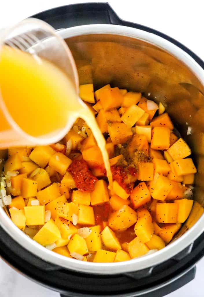 Pouring stock into an instant pot filled with cubed squash