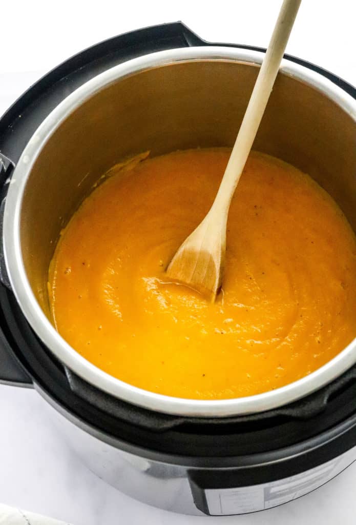 Blended butternut squash soup in an instant pot with a light wooden spoon inside the pot dipped in the soup