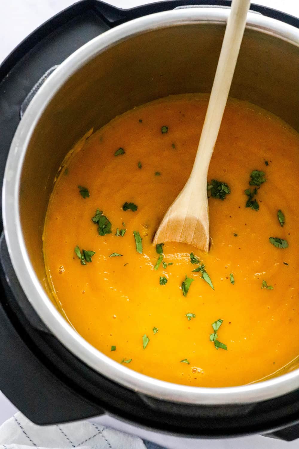 Butternut squash soup in an instant pot with torn cilantro on top of it and a light coloured wooden spoon in the pot. 