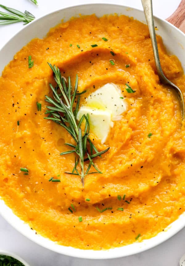Round white serving bowl filled with mashed butternut squash with a piece pf rosemary in the middle of it