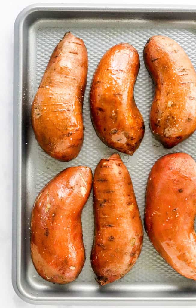Sliced sweet potatoes, cut side down on a silver baking sheet