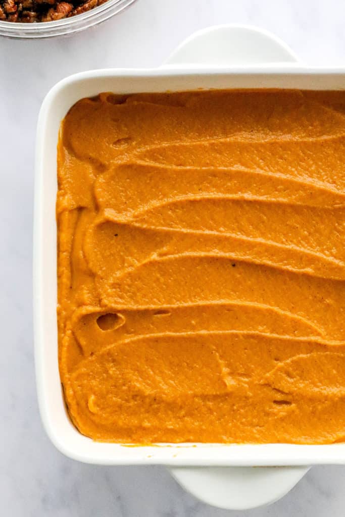 Blended sweet potato spread out in a white squash dish with a bowl of pecan crumble behind it