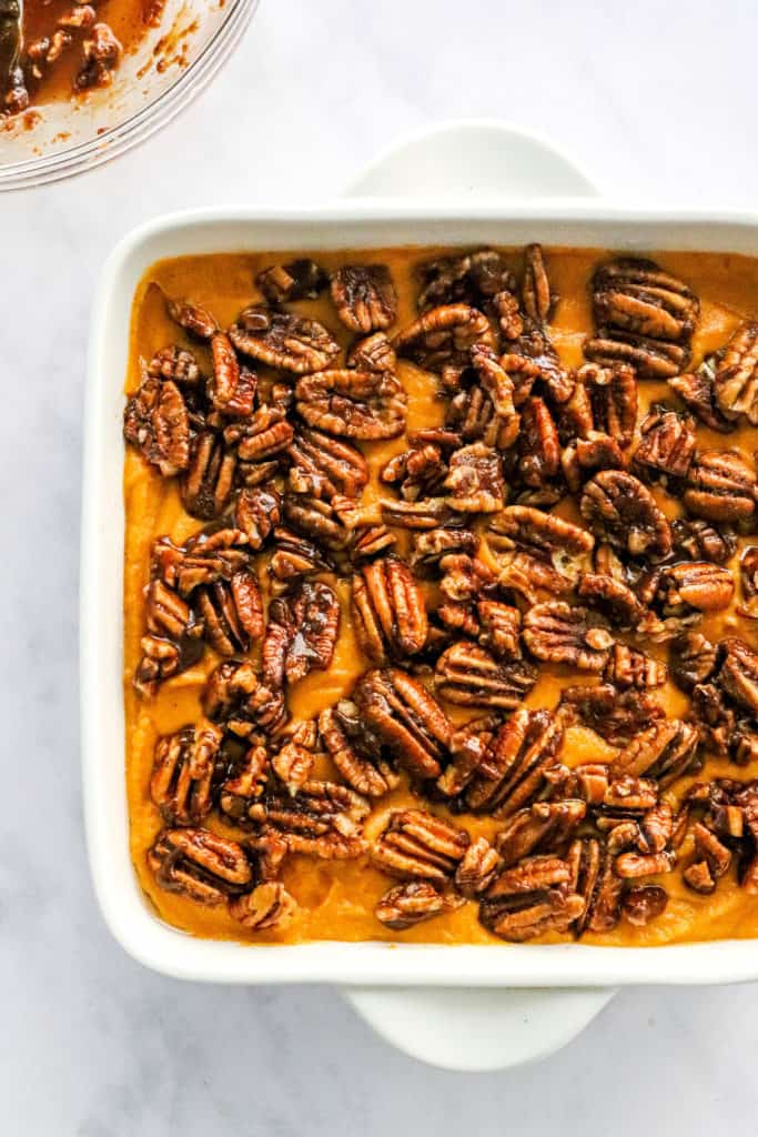 Uncooked sweet potato casserole with pecan topping in a square white baking dish on a marble counter