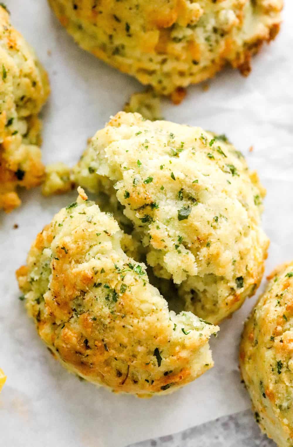 Fluffy herb and cheese biscuit pulled apart with more biscuits behind it. 