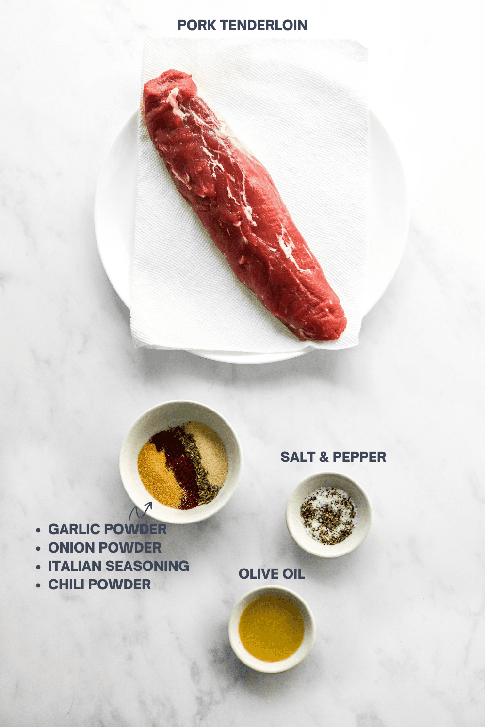Raw tenderloin on a round white plate with a small round bowl of seasoning, bowl of salt and pepper and a bowl of olive oil in front of it on a marble surface with labels for each ingredients next to them. 
