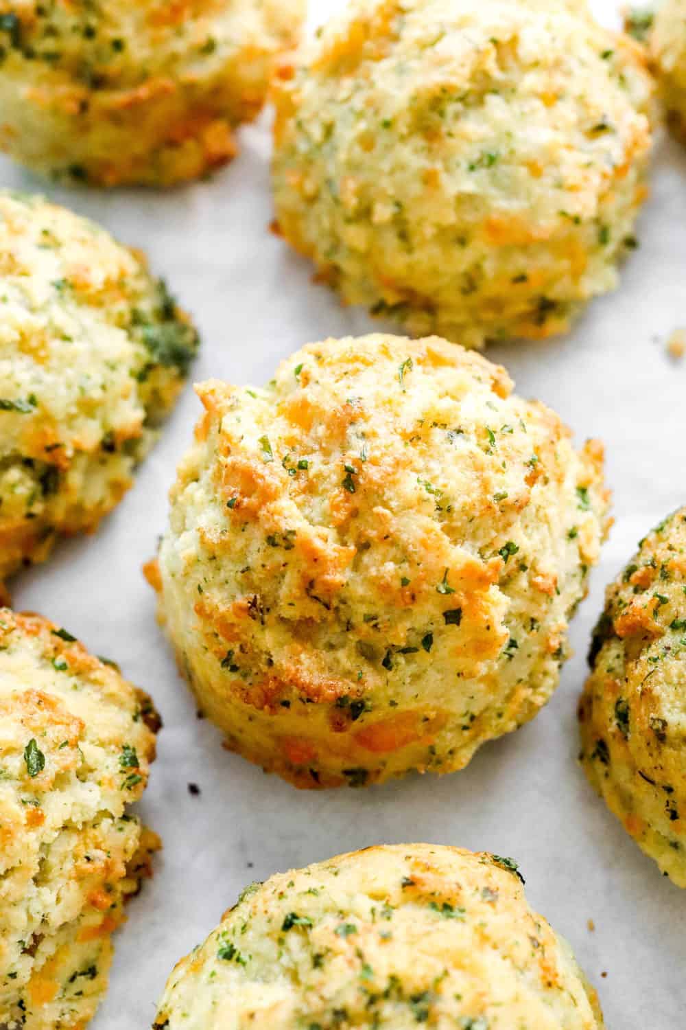 Air FRYER cheddar biscuits spread out on white parchment paper with green herbs sprinkled on top of them. 
