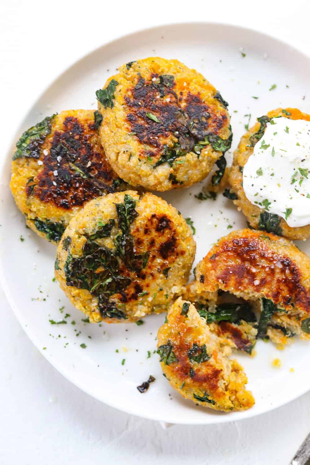 Kale and squash quinoa patties on a round white plate with yogurt on top of one of them. 